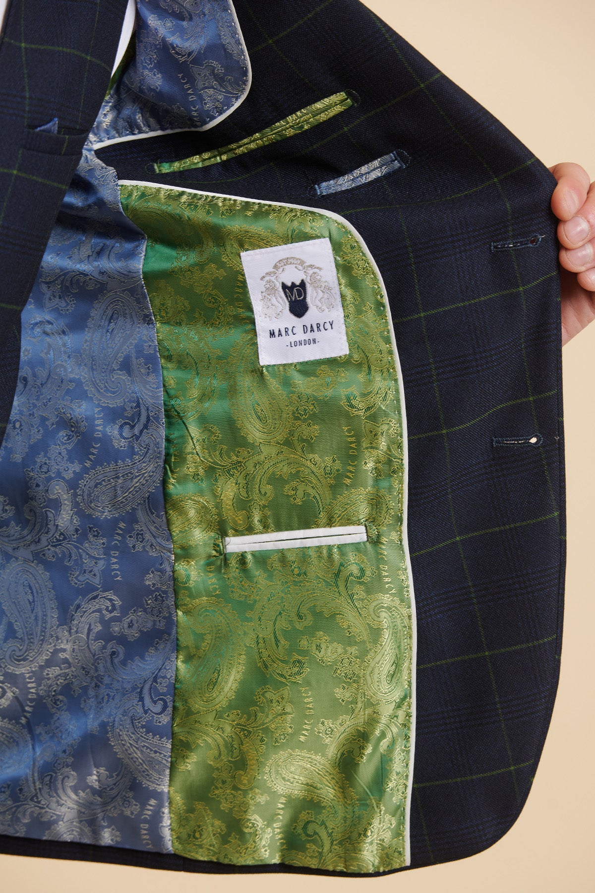 A hand opens a men's Everton Collection Beto In EDINSON Navy Green Check Two Piece Suit by Marc Darcy, revealing its blue and green paisley lining and a white "Marc Darcy" label.