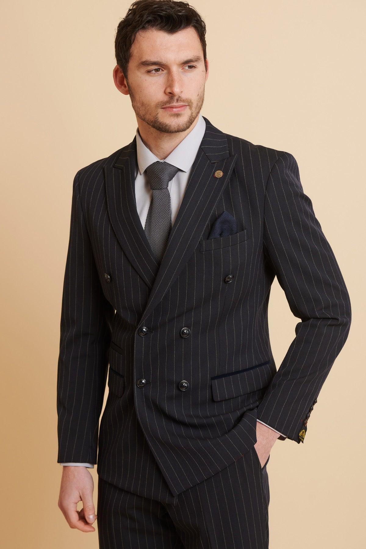A man wearing the Marc Darcy ROCCO Navy Pinstripe Double Breasted Blazer with a grey tie and pocket square stands against a tan background.