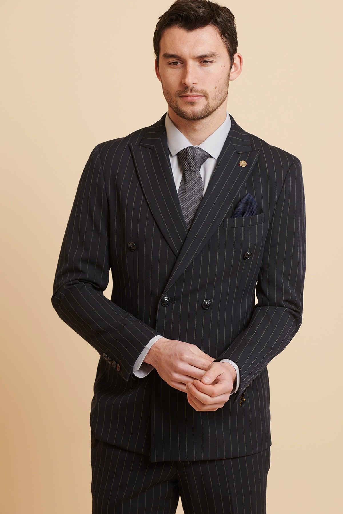 A man in the Marc Darcy ROCCO Navy Pinstripe Double Breasted Blazer, styled with a grey tie and pocket square, stands against a cream background.