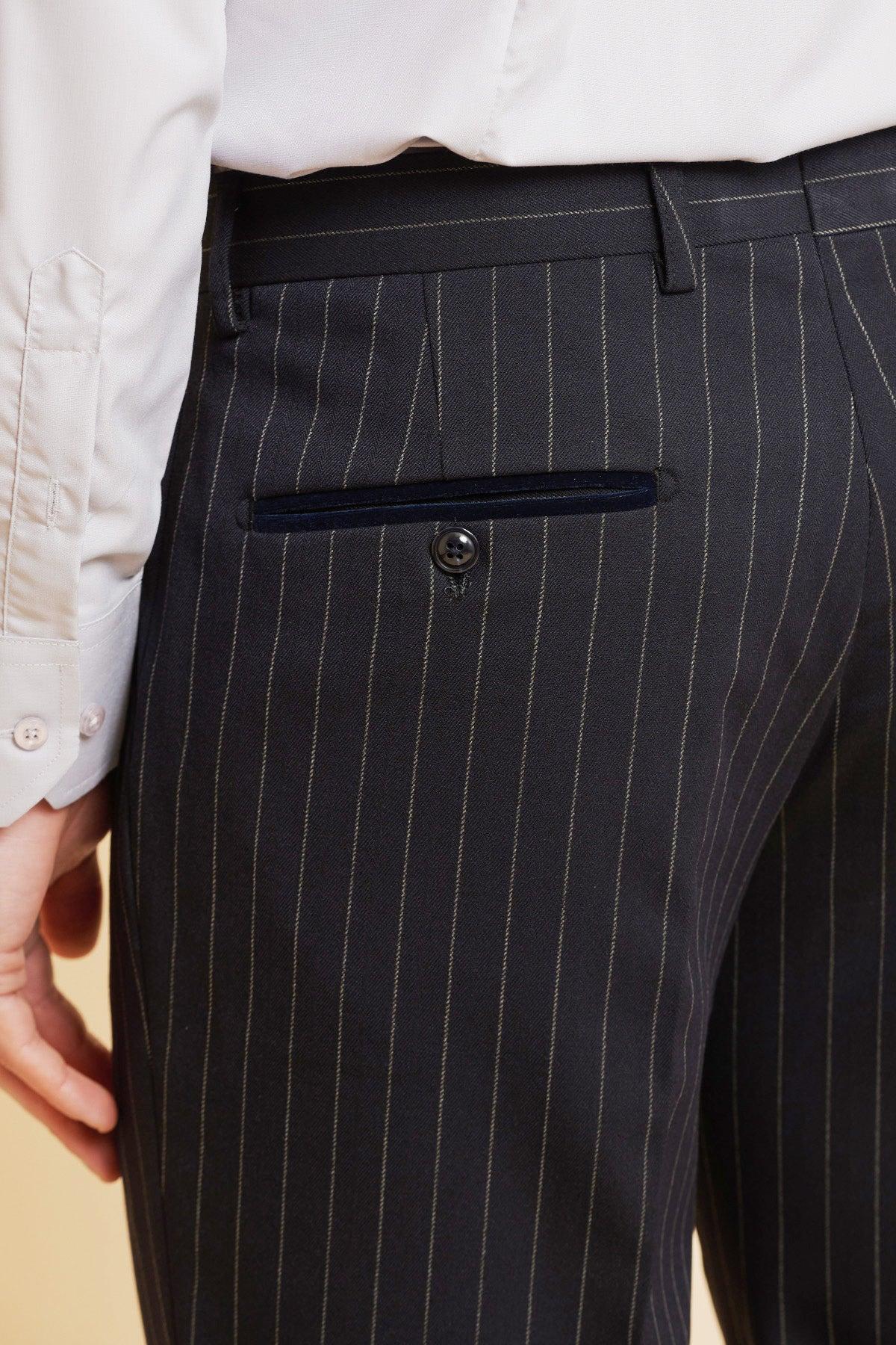 A close-up shows a person wearing Marc Darcy's ROCCO Navy Pinstripe Trousers with a white dress shirt. One hand is near the pants pocket, which has a button and a neat horizontal slit.