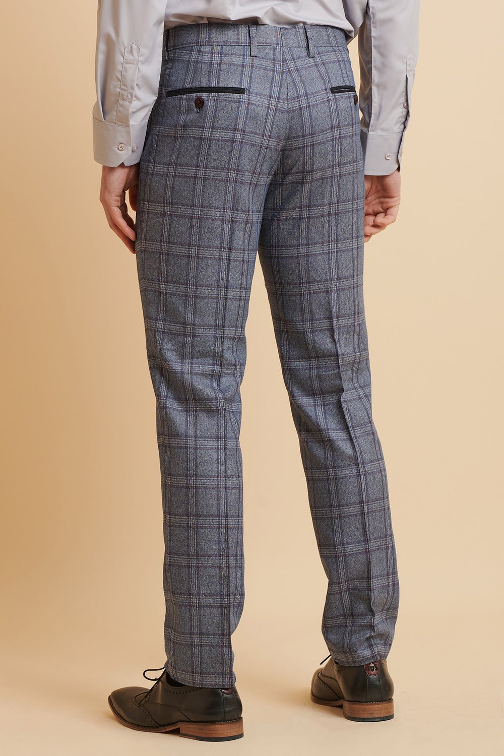 A person wearing marcdarcy ABBOTT Blue Tweed Check Trousers, a light dress shirt, and black shoes stands against a beige backdrop. The rear view highlights the trousers’ blue check pattern and back pockets.