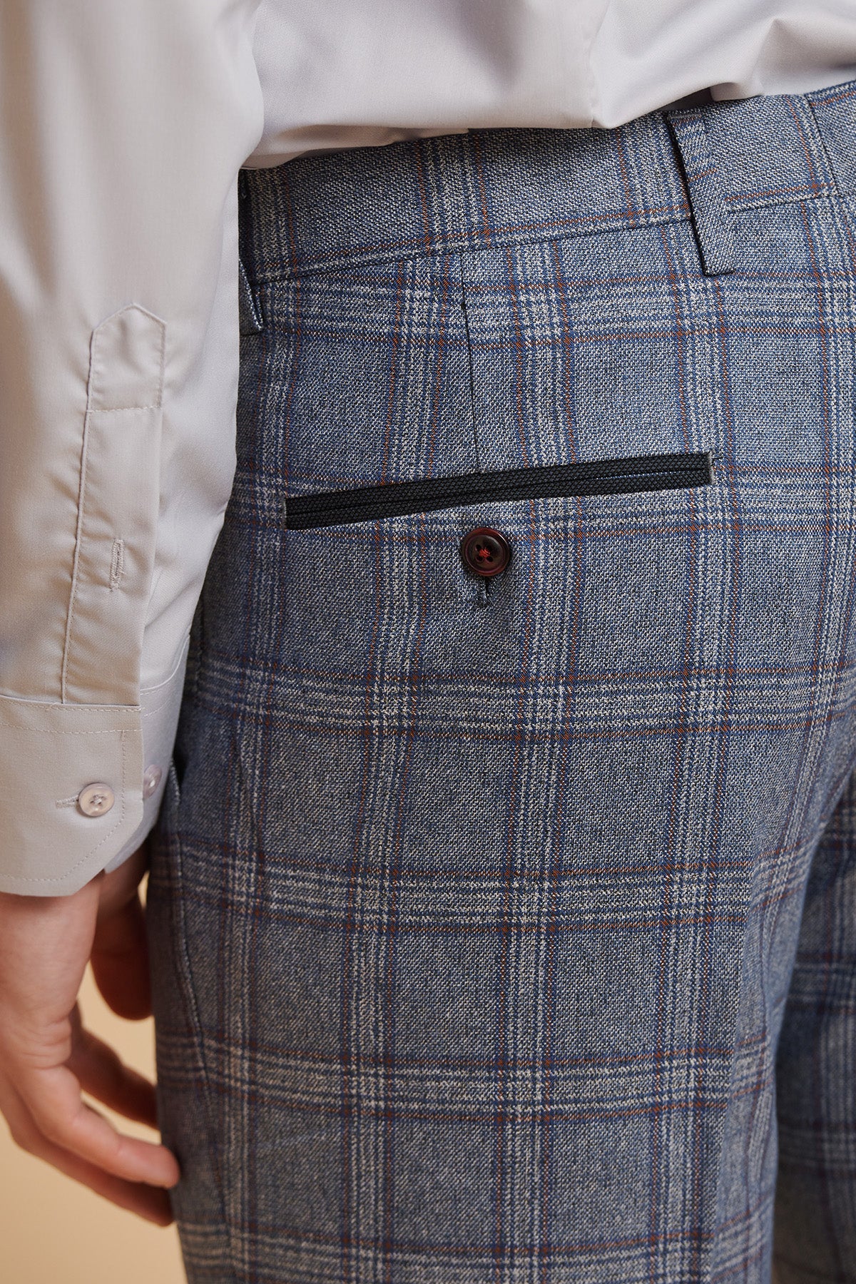A close-up of a person wearing marcdarcys ABBOTT Blue Tweed Check Trousers with a buttoned back pocket, paired with a white dress shirt. Their arm is relaxed by their side.