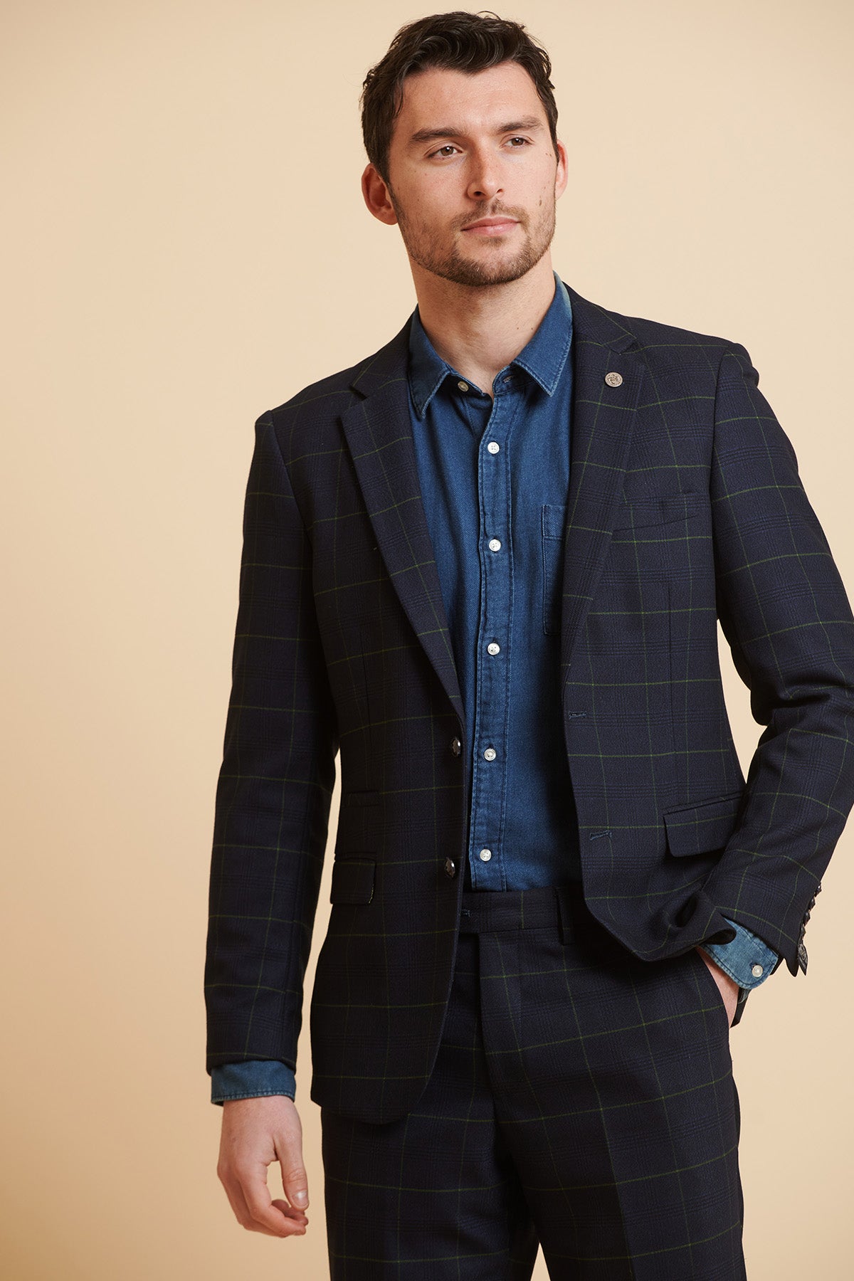 Jordan Pickford wears the Marc Darcy Edinson Navy Green Check Blazer from The Everton Collection, styled with a denim shirt and his hand in his pocket.