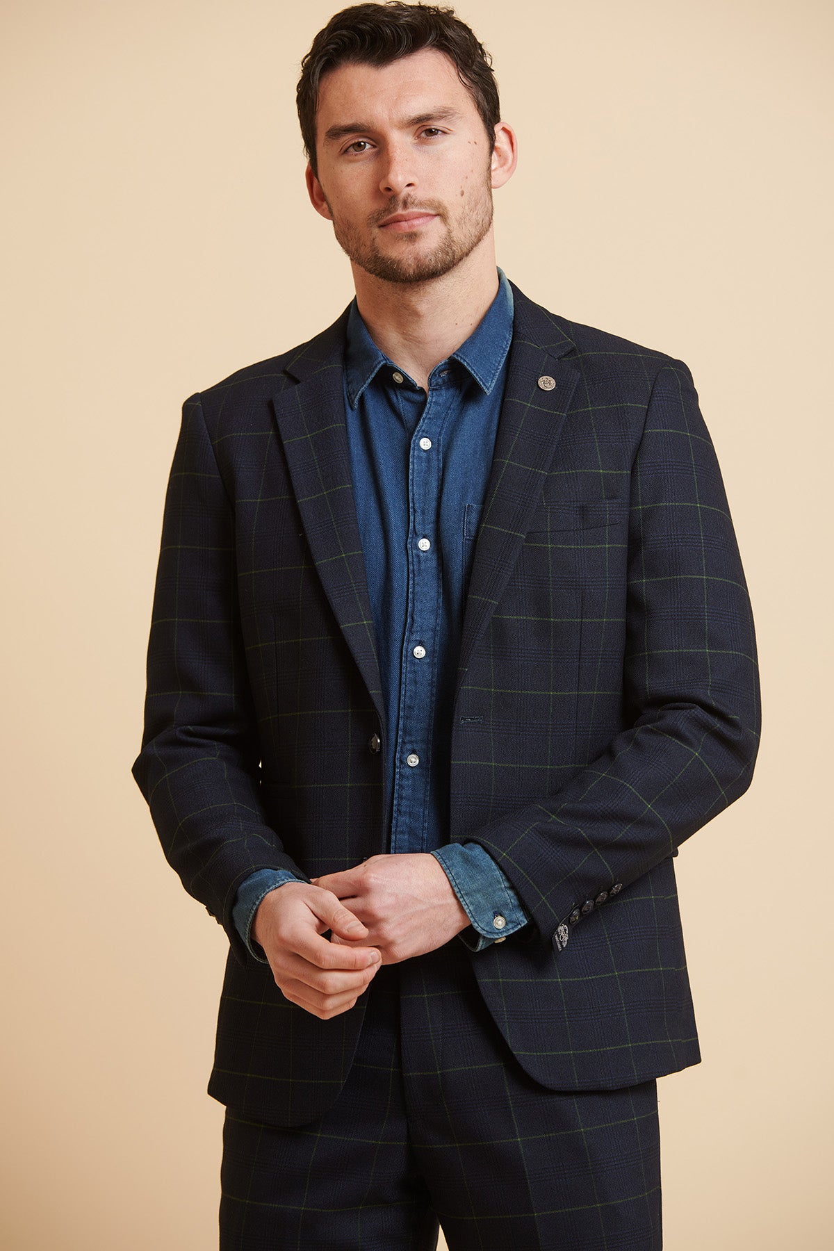 A man with short dark hair and light stubble models the Marc Darcy EDINSON Navy Green Check Blazer in a slim tailored fit over a blue denim shirt, standing against a plain beige background.