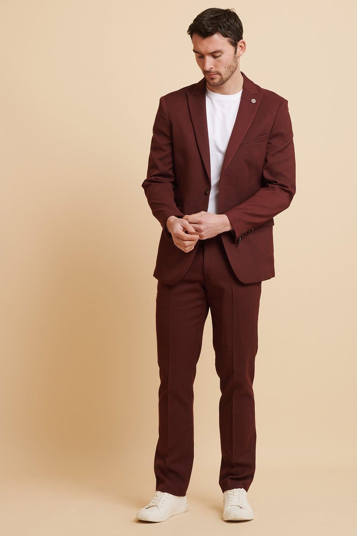 A man poses against a beige background, wearing the marcdarcy MAX Wine Two Piece Suit with a slim fit blazer, styled with a white t-shirt and white sneakers, looking down with his hands in front of him.
