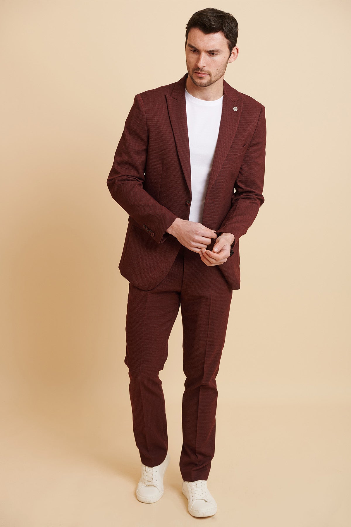 A man in the marcdarcy MAX - Wine Tailored Blazer and a white t-shirt stands against a cream backdrop, adjusting his blazer cuffs.