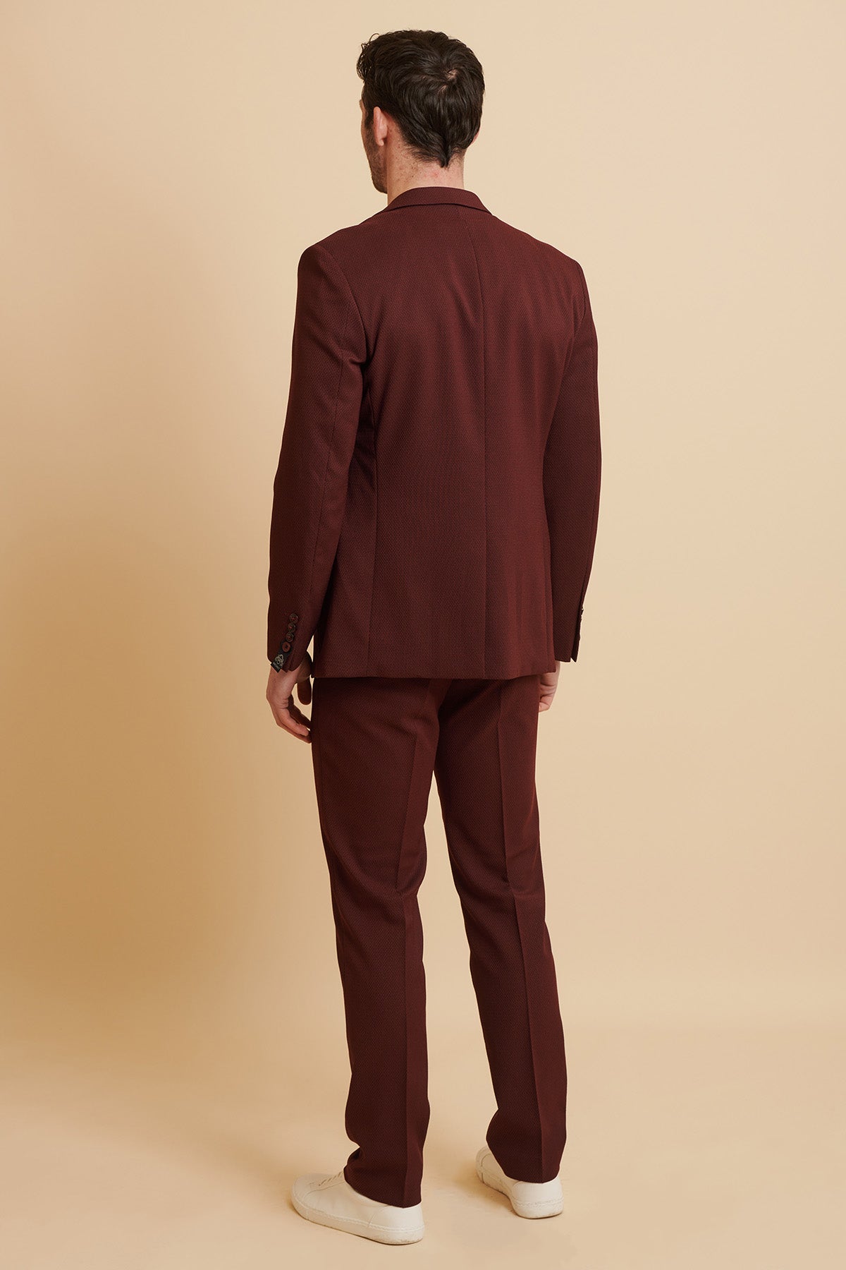 A man faces away from the camera, wearing the marcdarcy MAX Wine Tailored Blazer and white sneakers, set against a beige background.