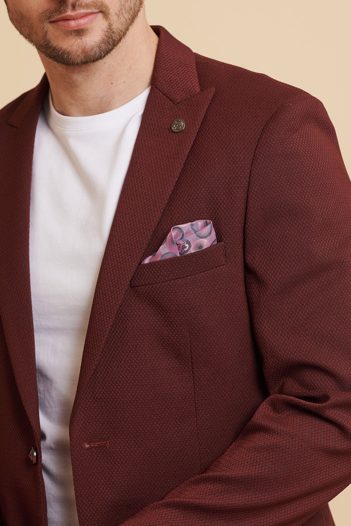 A man wears the marcdarcy MAX - Wine Tailored Blazer over a white t-shirt, with a pink patterned pocket square in the chest pocket. His face is partly visible against a beige background.