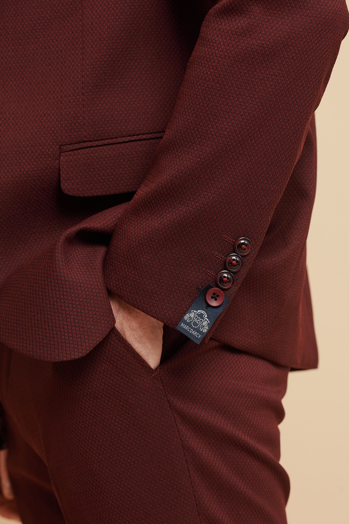 A person wears the marcdarcy MAX - Wine Tailored Blazer, standing with one hand in their pocket. The close-up highlights the sleeve's three buttons and brand tag near the cuff, showcasing this stylish slim fit blazer.