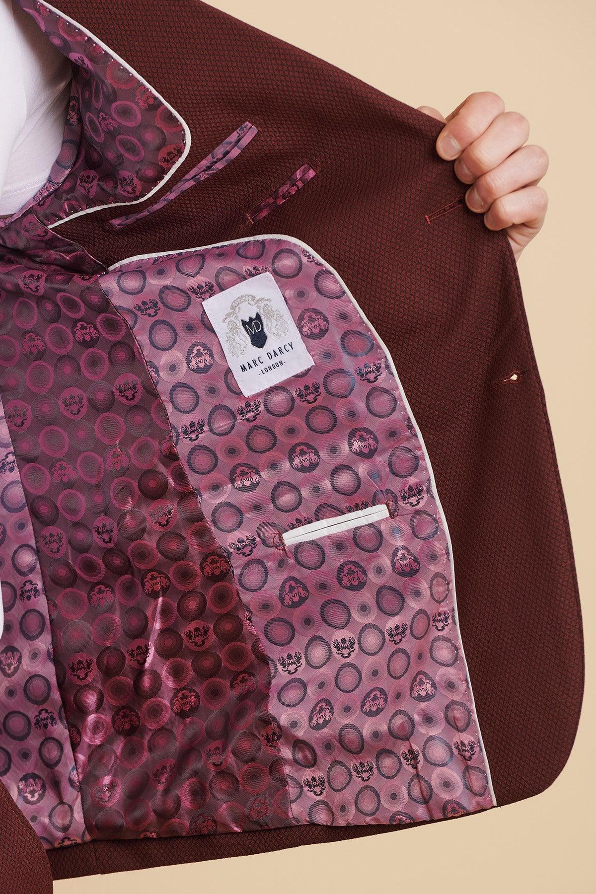 A person opens a MAX - Wine Two Piece Suit by marcdarcy, showing a slim fit blazer with pink and purple patterned lining, circular designs, and the marcdarcy label. A camouflage pocket square adds a distinctive flair.