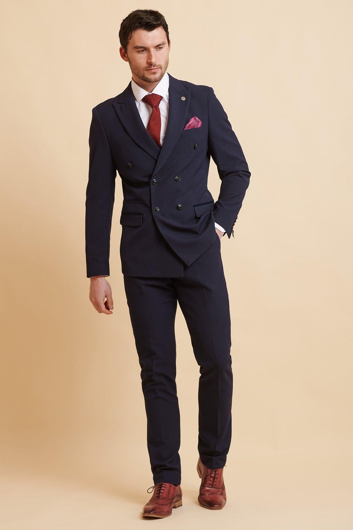 A man wears the Official West Ham United Club Suit, the BROMLEY Navy Double Breasted Suit by Marc Darcy, paired with a white shirt, red tie, burgundy shoes, and a maroon pocket square.