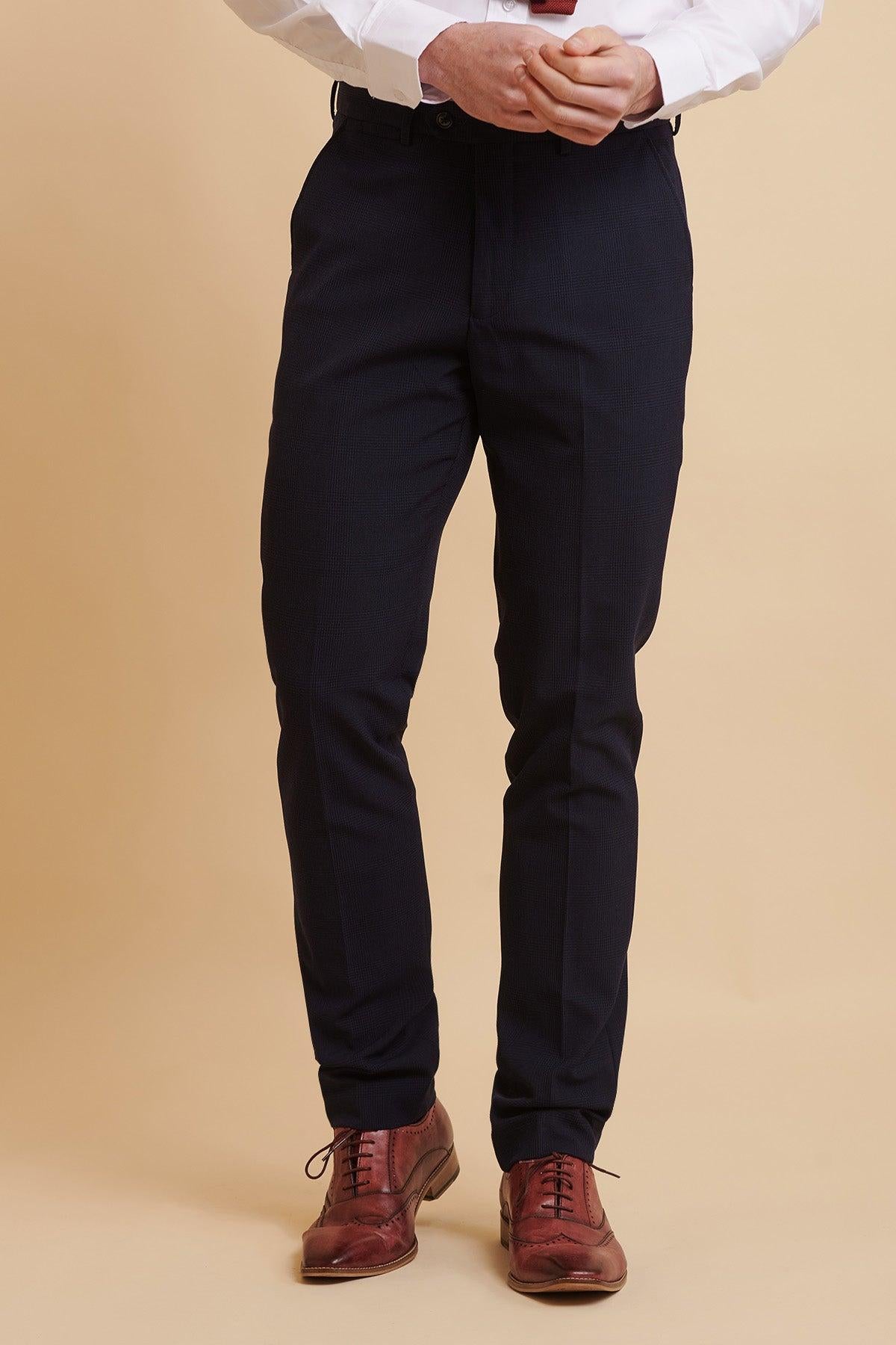 Man wearing the Official West Ham United Club Suit, BROMLEY Navy Double Breasted Suit by Marc Darcy, paired with a white dress shirt and brown oxford shoes on a tan background.