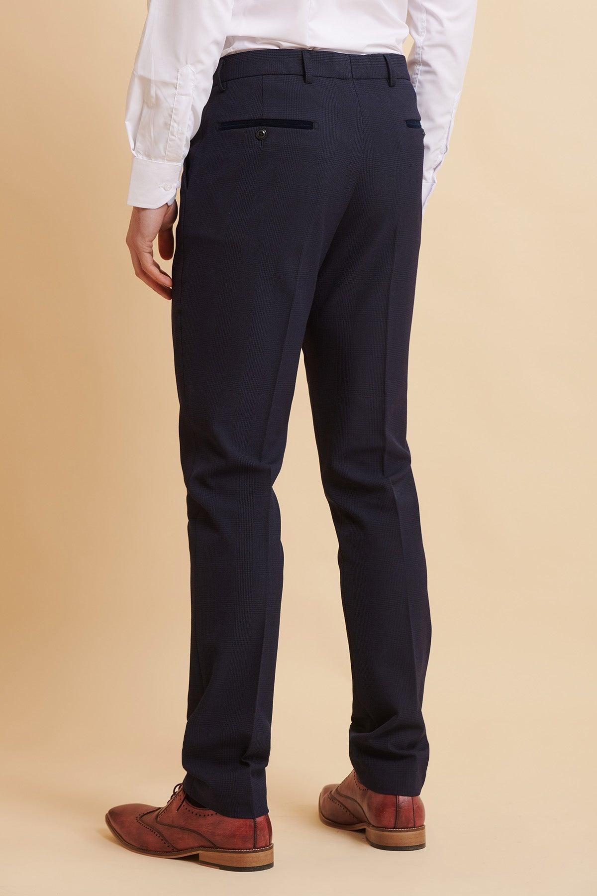 A man wears the Marc Darcy Official West Ham United Club Suit—BROMLEY Navy Double Breasted Suit—with navy slacks, a white dress shirt, and brown leather shoes, featuring subtle Prince of Wales check detailing.
