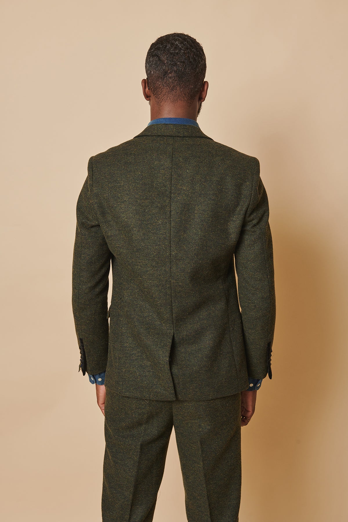 A man faces away from the camera, wearing the marcdarcy MARLOW Olive Green Tweed Blazer with matching trousers, set against a plain beige background.