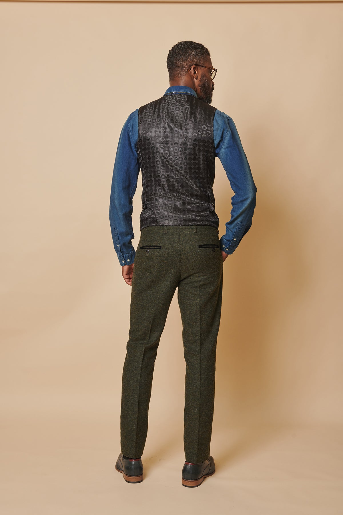 Man wearing a marcdarcy MARLOW Olive Green Tweed Three Piece Suit, featuring a blue denim shirt and dark patterned waistcoat, viewed from behind.