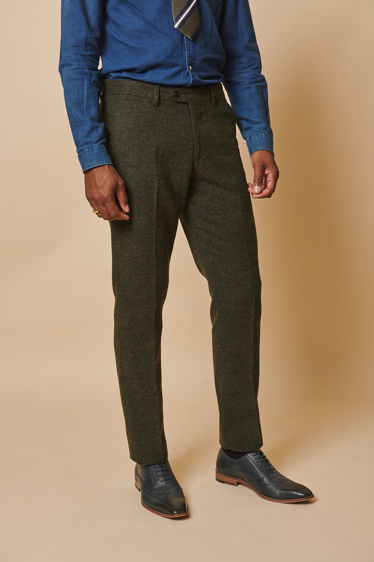 A man in a blue dress shirt, striped tie, marcdarcy MARLOW Olive Green Tweed Trousers, and black dress shoes stands against a plain beige background. His head is not visible in the image.