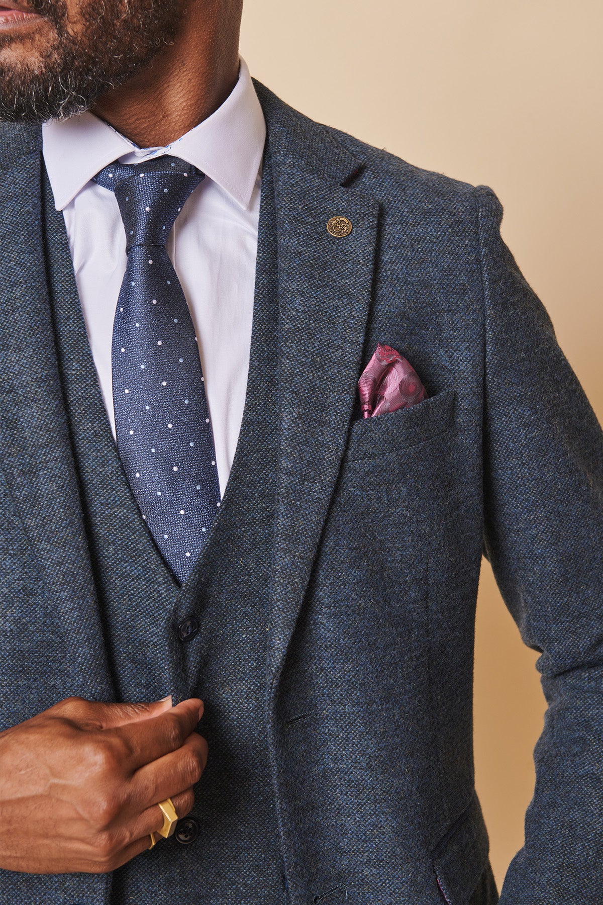 A man wears the marcdarcy MARLOW Blue Tweed Blazer with a slim fit, paired with a white shirt, blue polka dot tie, pink patterned pocket square, and gold ring.