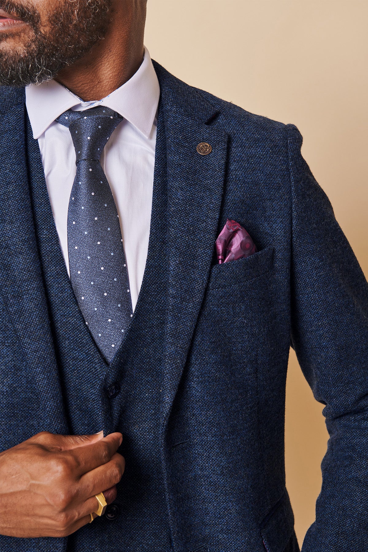 A man wearing the marcdarcy MARLOW Navy Tweed Blazer with a white shirt, polka dot tie, and purple pocket square adjusts his jacket. Only the lower half of his face and torso are visible.