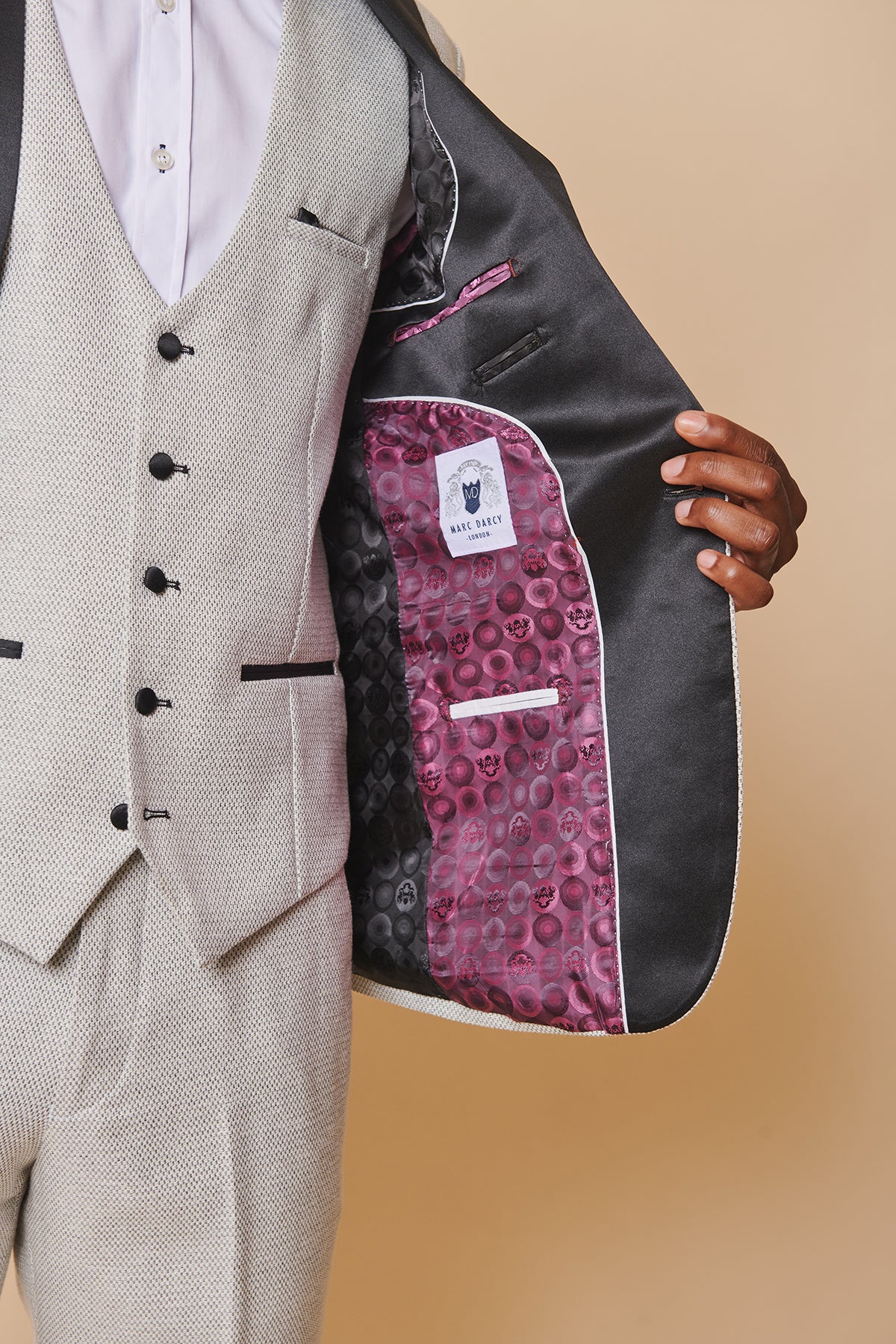 The marcdarcy SPENCER Stone Tux Lapel Three Piece Suit is shown with the jacket held open, revealing a black satin and pink patterned lining with the brand label, worn over a matching waistcoat featuring black buttons.