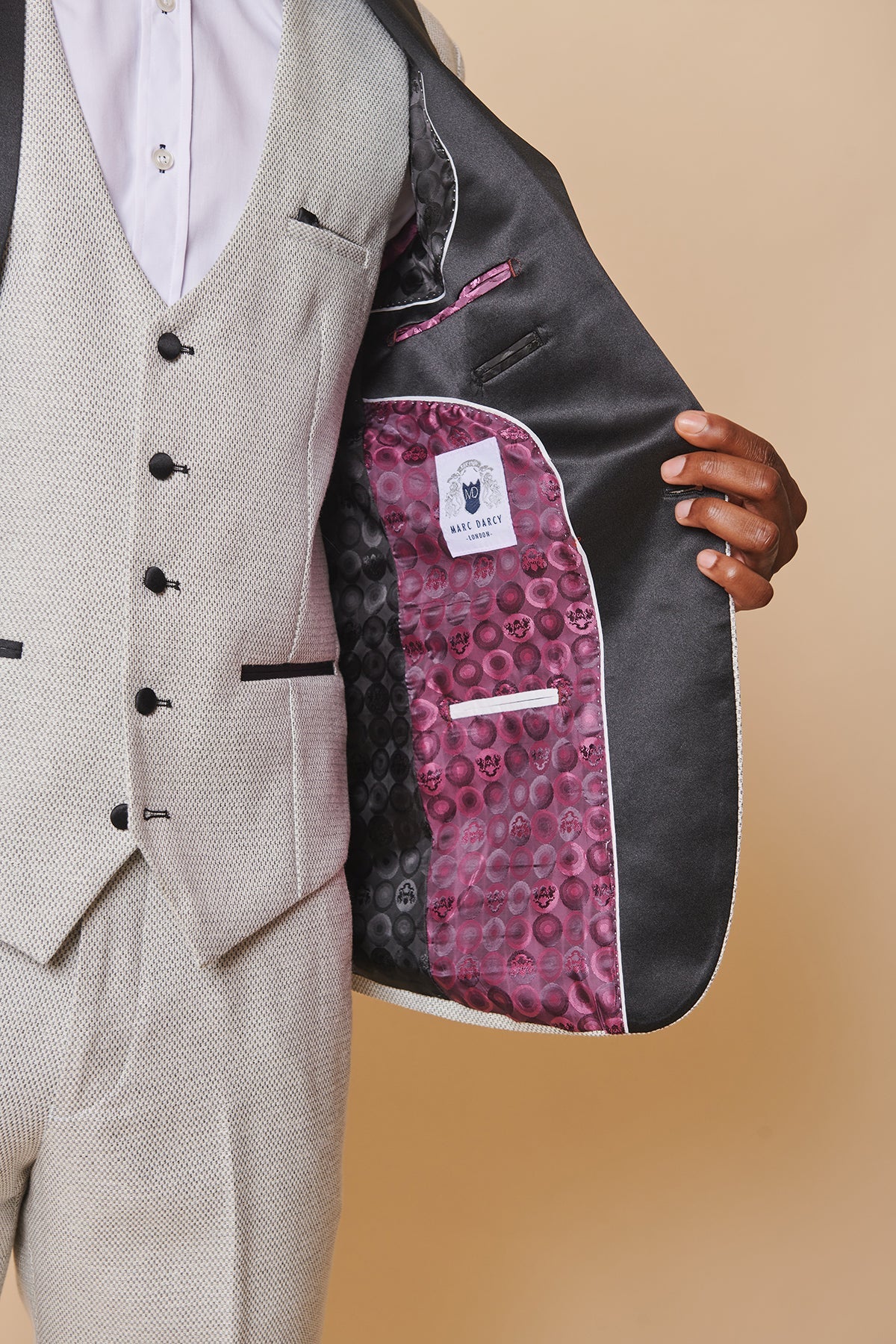 Close-up of a man in marcdarcy’s The Everton Collection | Ashley Young In SPENCER Stone Tux Lapel Suit: light grey textured three-piece with white shirt. Open jacket reveals dark grey satin lining with vibrant pink and black circular design.