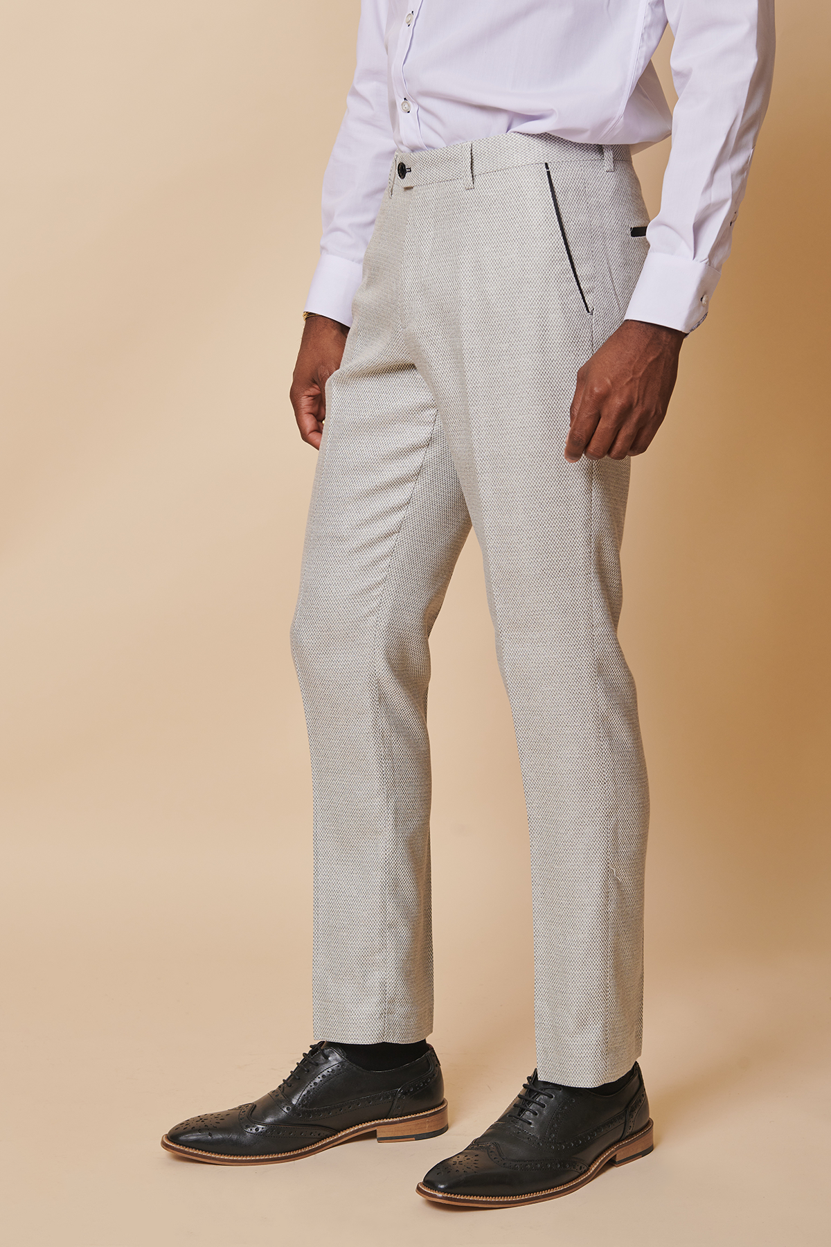 A man models marcdarcy’s SPENCER - Stone Trousers with a white dress shirt and black shoes against a beige background, his face not visible.
