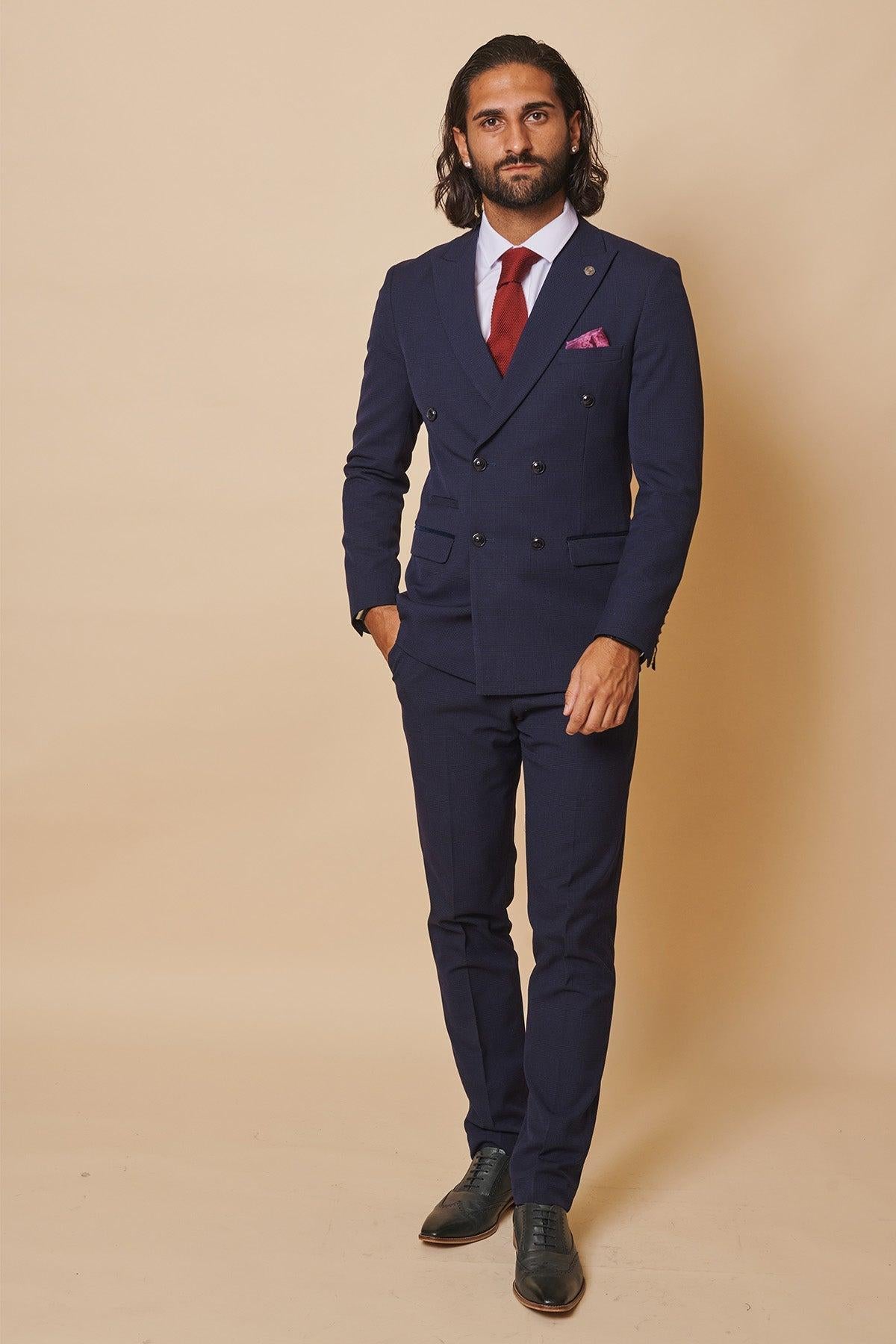 Former Sunderland footballer Michael Gray stands against a beige background wearing the Marc Darcy Bromley Navy Double-Breasted Suit, paired with a white shirt, red tie, pink pocket square, and black shoes.