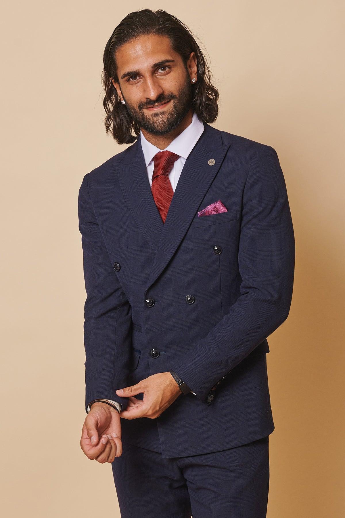 Former Sunderland footballer Michael Gray wears the Marc Darcy Bromley Navy Double-Breasted Suit, paired with a red tie and pink pocket square, as he adjusts his cuff against a beige backdrop.