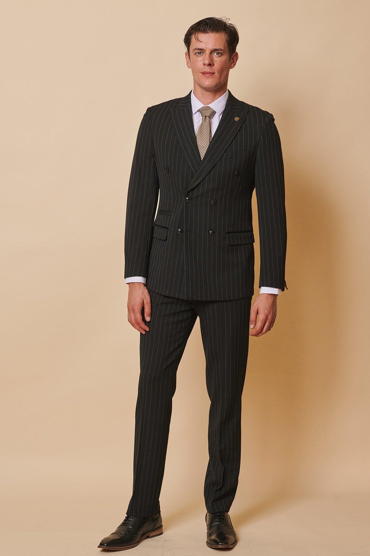 Luca Toolan as Mason Radcliffe wears the Marc Darcy ROCCO black pinstripe double-breasted two-piece suit with a tailored fit, white shirt, and light tie, standing against a beige background with a neutral expression.