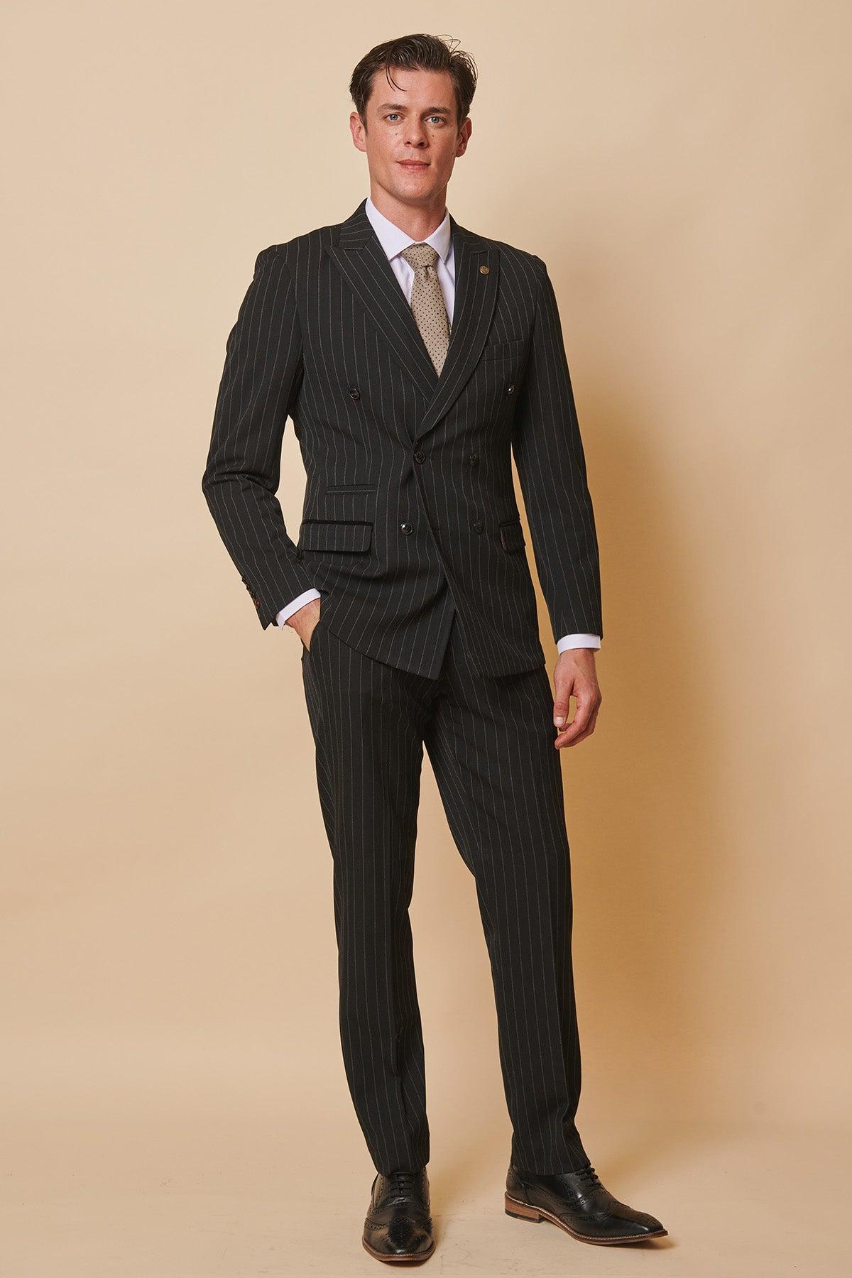 Coronation Street’s Mason Radcliffe (Luca Toolan) wears a Marc Darcy ROCCO black pinstripe double breasted two piece suit with a white shirt and patterned tie, standing with his hand in his pocket.