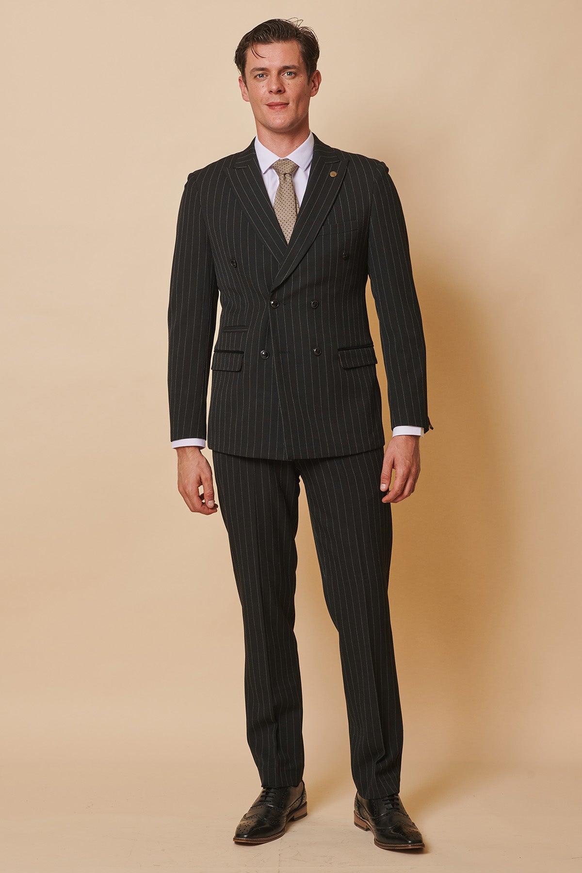 Luca Toolan (as Mason Radcliffe) smiles against a beige background, wearing Marc Darcys ROCCO black pinstripe double-breasted suit, white shirt, tan tie, and black dress shoes with short, neat hair.