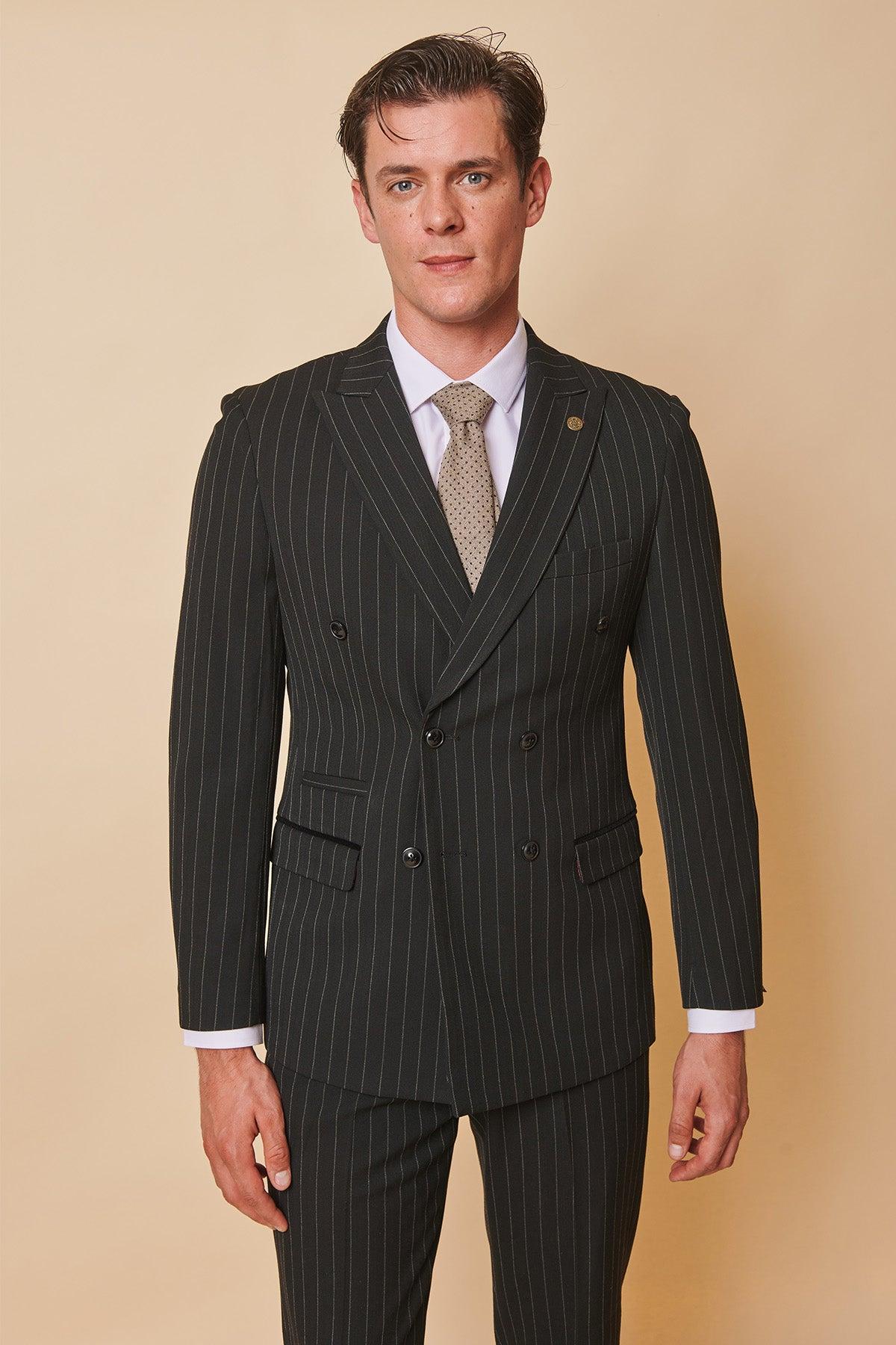 Luca Toolan as Mason Radcliffe from Coronation Street wears the Marc Darcy ROCCO Black Pinstripe Double Breasted Two Piece Suit, styled with a white shirt and beige patterned tie, standing against a beige background.