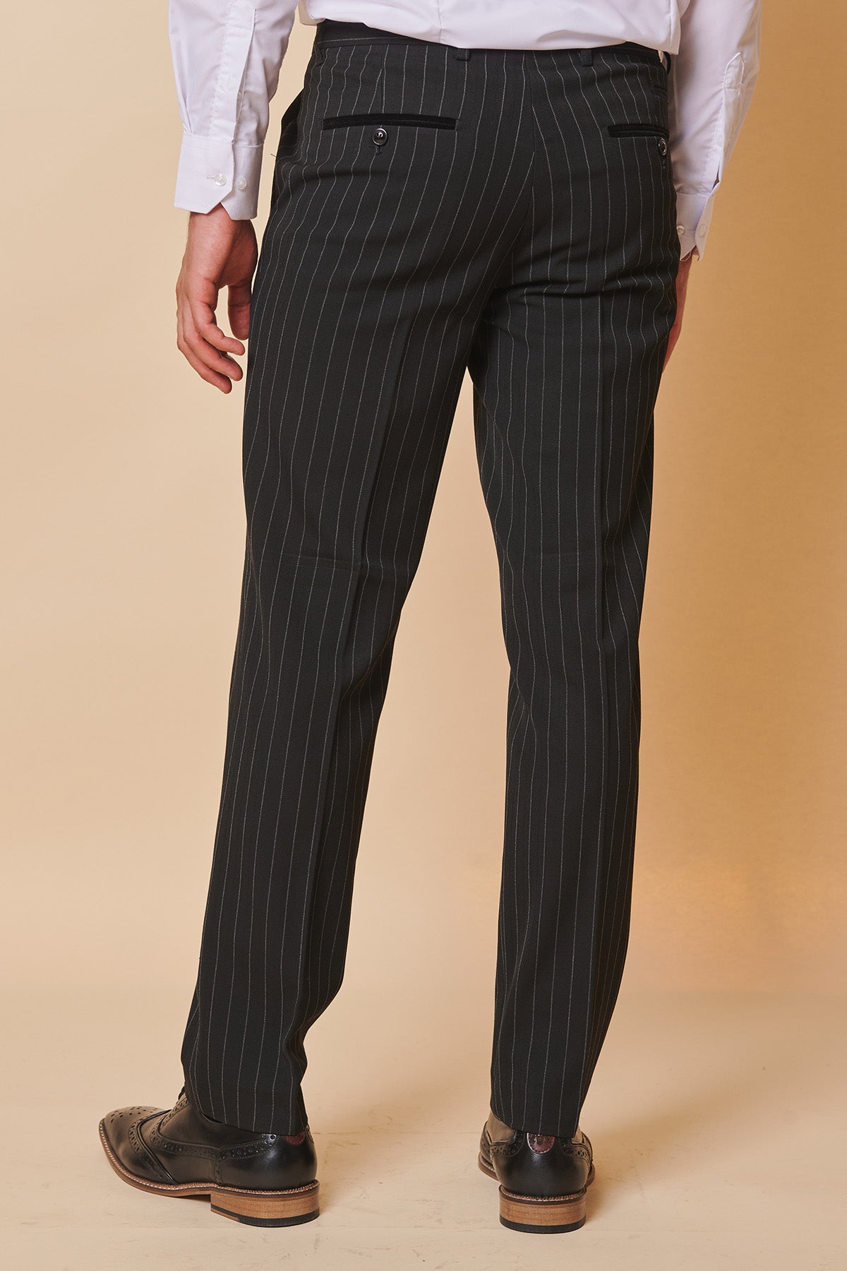 Back view of a man wearing Marc Darcy's ROCCO Black Pinstripe Trousers, paired with a white dress shirt and black wingtip shoes.