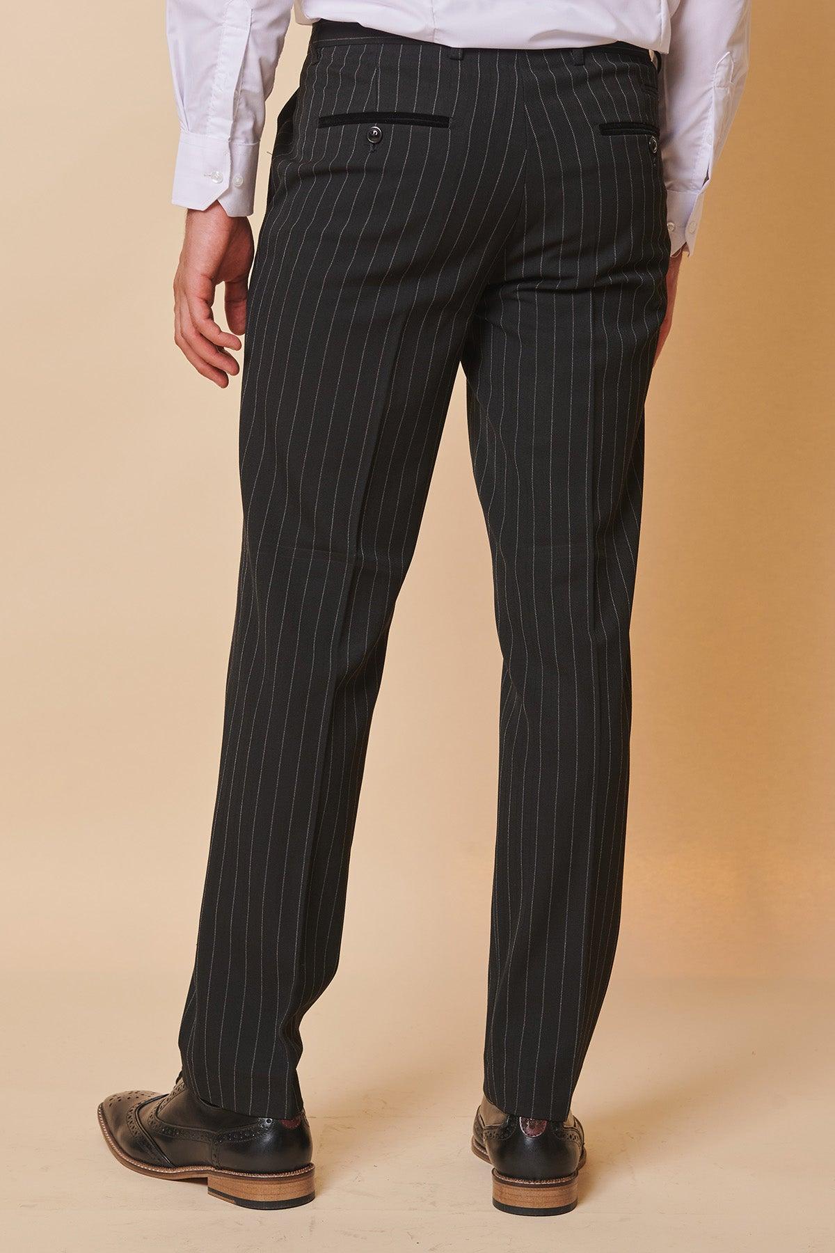 A person wearing Marc Darcy’s ROCCO Black Pinstripe Double Breasted Suit, as seen on Luca Toolan (Mason Radcliffe, Coronation Street), stands with their back to the camera against a plain beige background.