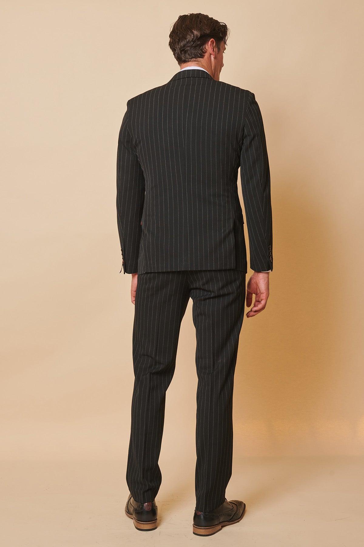 Coronation Streets Mason Radcliffe (Luca Toolan) wears a Marc Darcy ROCCO Black Pinstripe Double Breasted Two Piece Suit, styled with matching trousers and brown dress shoes against a beige background.