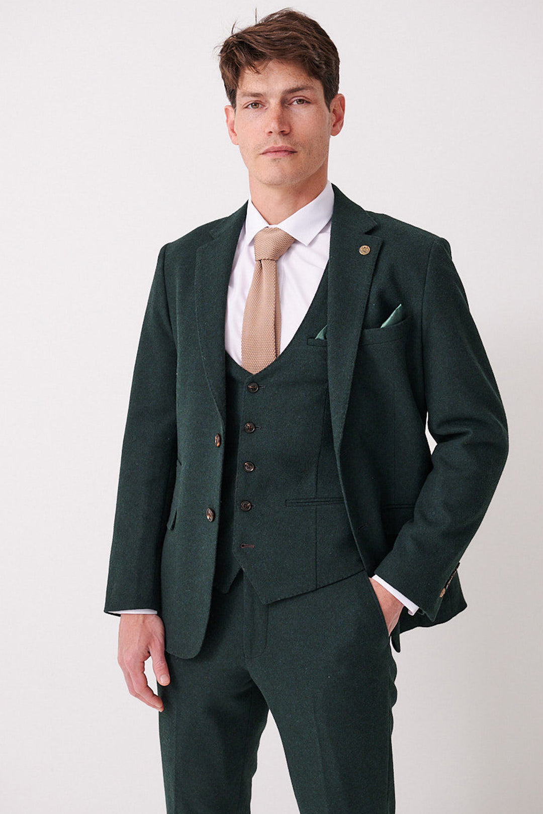 A man with short hair and a neutral expression stands against a white background, wearing the marcdarcy ARCHIE - Forest Tweed Blazer with a matching vest, white dress shirt, light brown tie, and one hand in his pocket.
