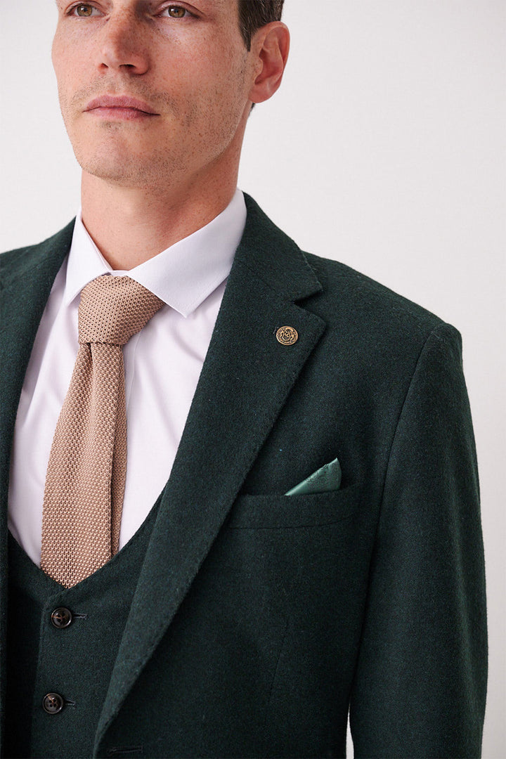 A man in the marcdarcy ARCHIE Forest Tweed Three Piece Suit, with a white shirt, beige textured tie, and green pocket square, shown from the shoulders up and facing slightly to the side.