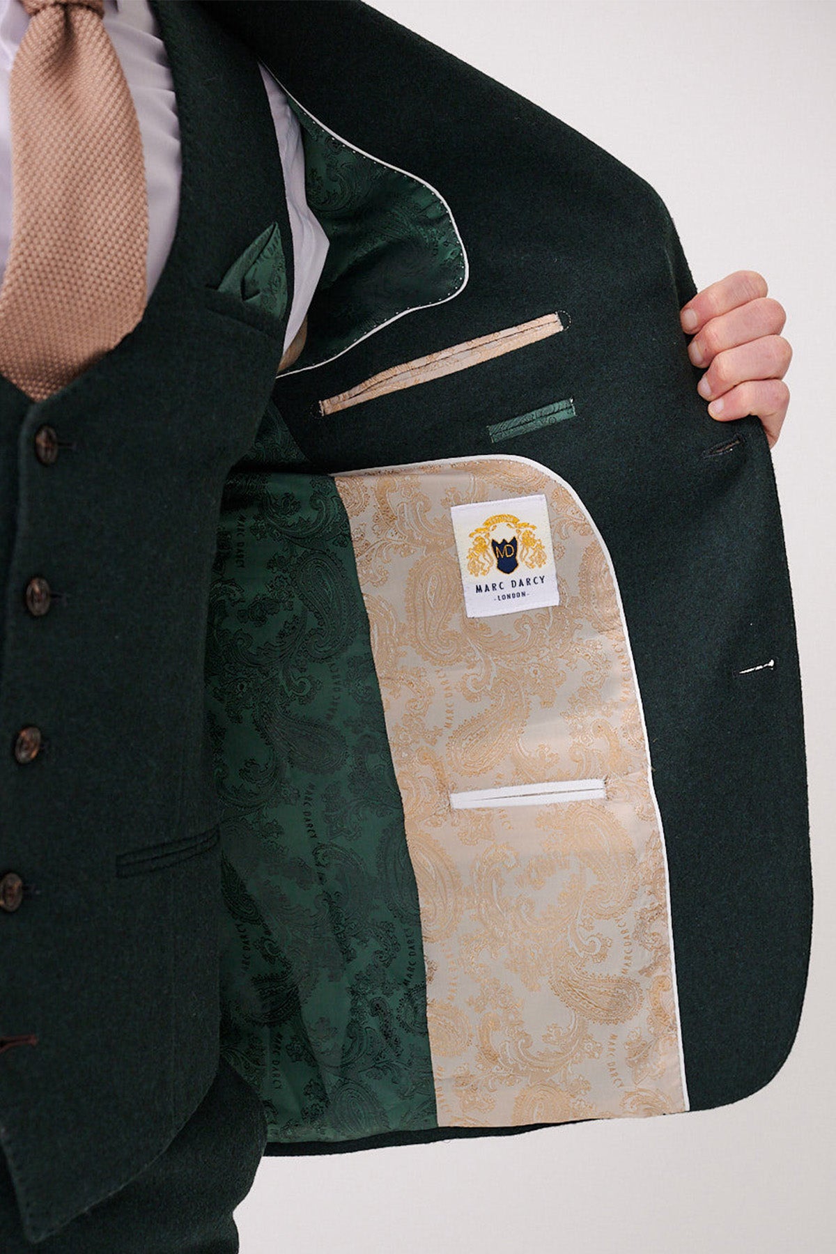 A person in a forest tweed ARCHIE blazer by marcdarcy with a beige tie holds open their jacket, showing off its light and dark green paisley lining and a white label with yellow detailing that reads marcdarcy.