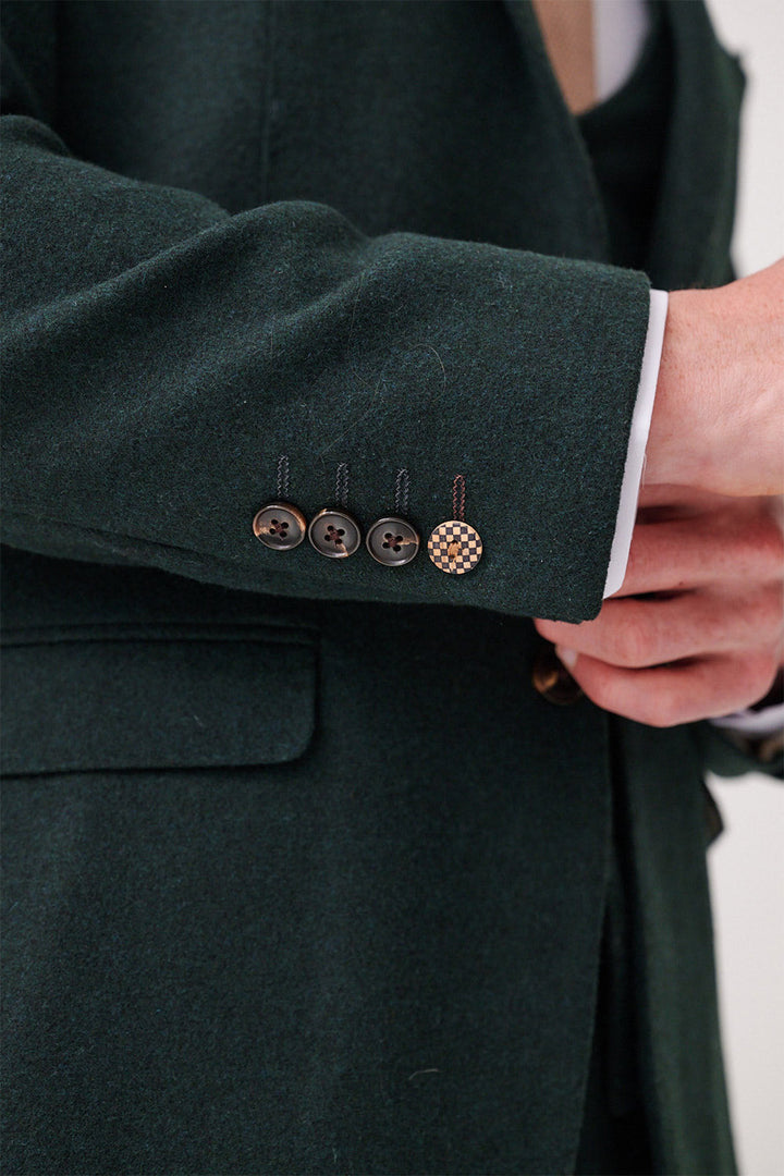A close-up of a man in marcdarcy’s ARCHIE - Forest Tweed Blazer adjusting the cuff, showing three black buttons and one unique Prince of Wales check button, with a brown tie and white shirt cuff partly visible.
