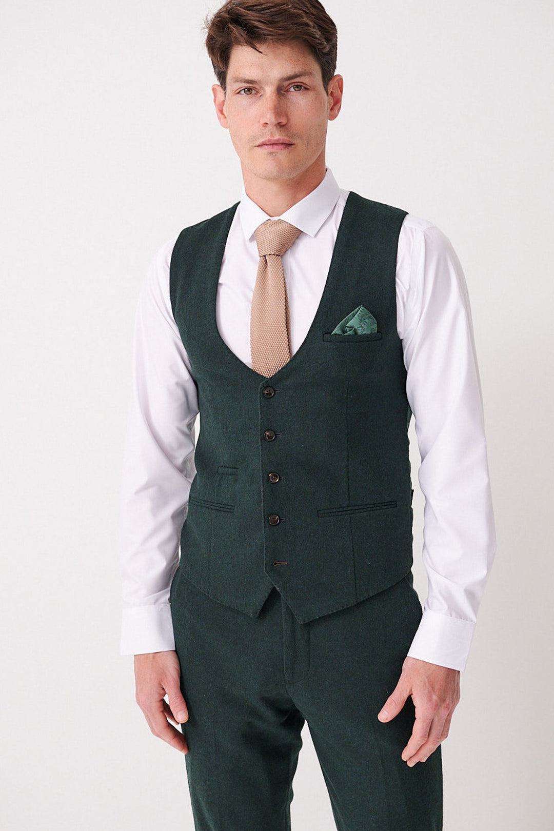 A man wears the Marc Darcy ARCHIE Forest Tweed Waistcoat with a slim fit, white shirt, tan tie, and green pocket square, standing against a plain light background.