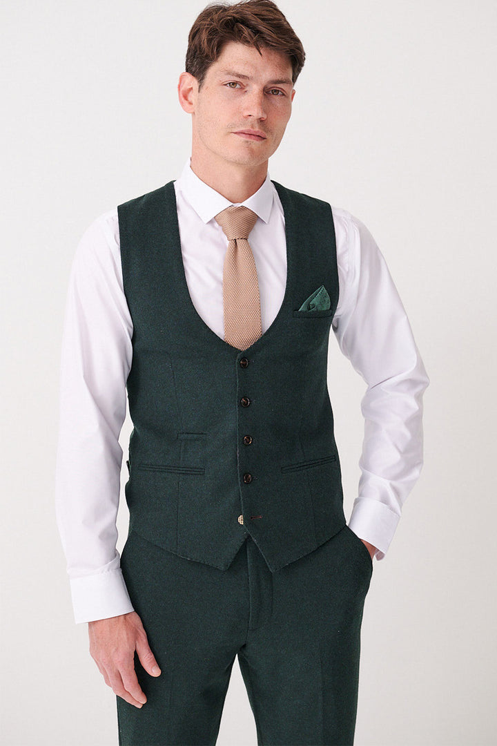 A man wears the Marc Darcy ARCHIE Forest Tweed Waistcoat with matching trousers, a white shirt, beige tie, and green pocket square, standing against a plain light background.