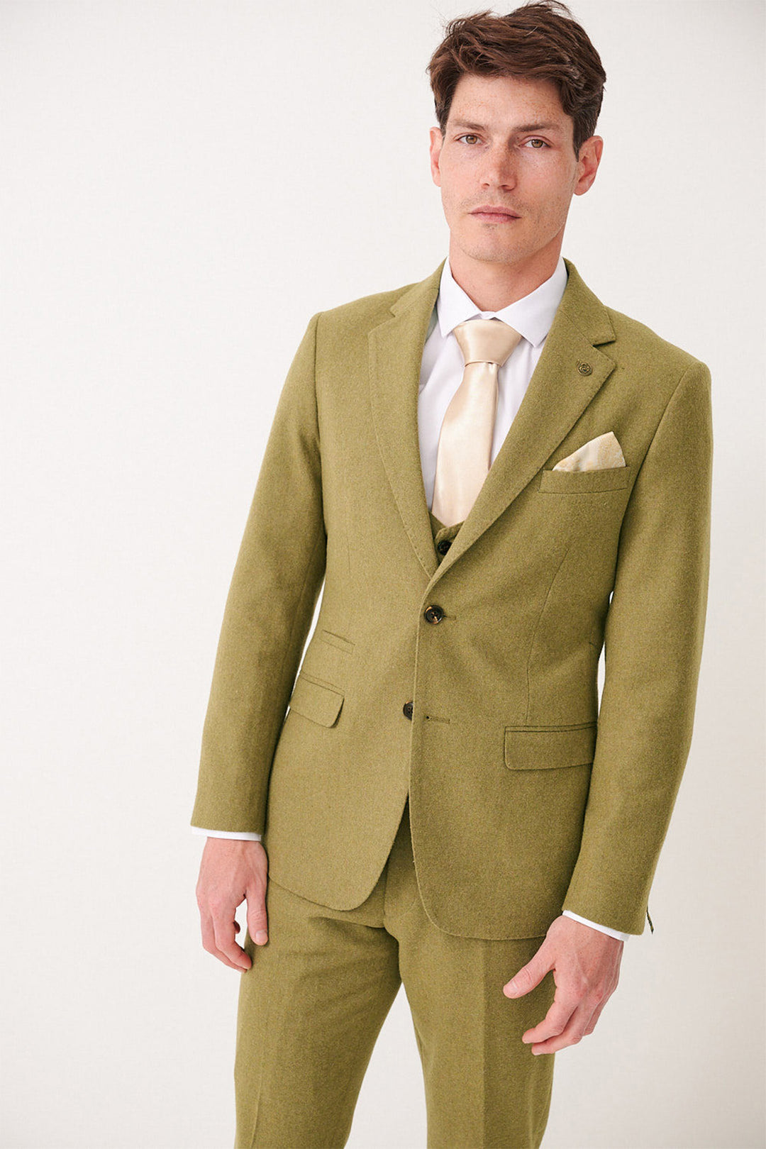 A man in the ARCHIE - Moss Tweed Three Piece Suit by marcdarcy with a cream tie and matching pocket square stands against a plain light background, facing the camera with a neutral expression.