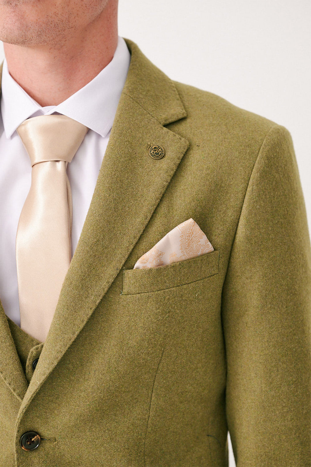 A person wearing the marcdarcy ARCHIE Moss Tweed Three Piece Suit, paired with a white dress shirt, cream tie, and matching patterned pocket square. The image is cropped to show only the chest and part of the face.