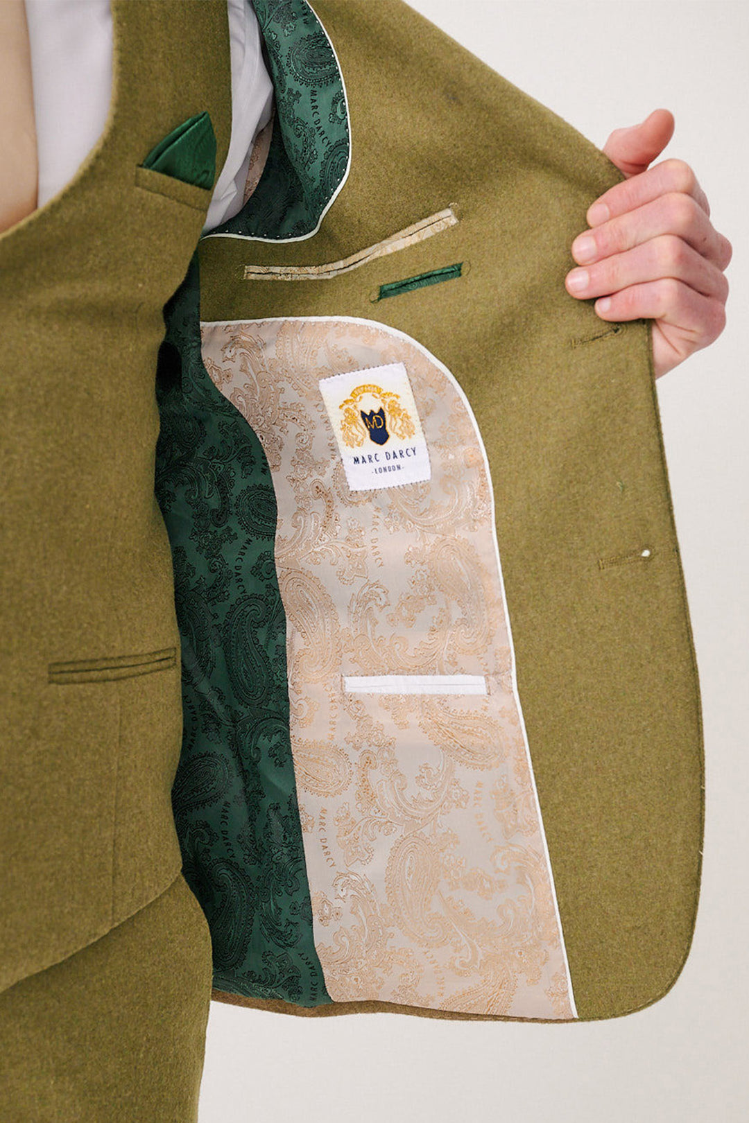 A person holds open the lapel of a marcdarcy ARCHIE Moss Tweed Three Piece Suit, showing a patterned green and beige paisley lining with a marcdarcy label sewn inside.