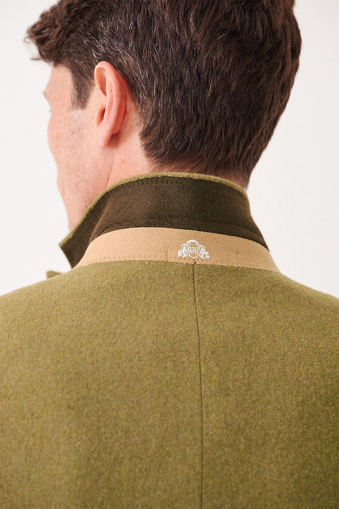 A close-up of a man's head and shoulders highlights the marcdarcy ARCHIE - Moss Tweed Three Piece Suit, featuring an olive green coat with a beige collar and small white embroidered emblem at the neck, styled for a slim fit.