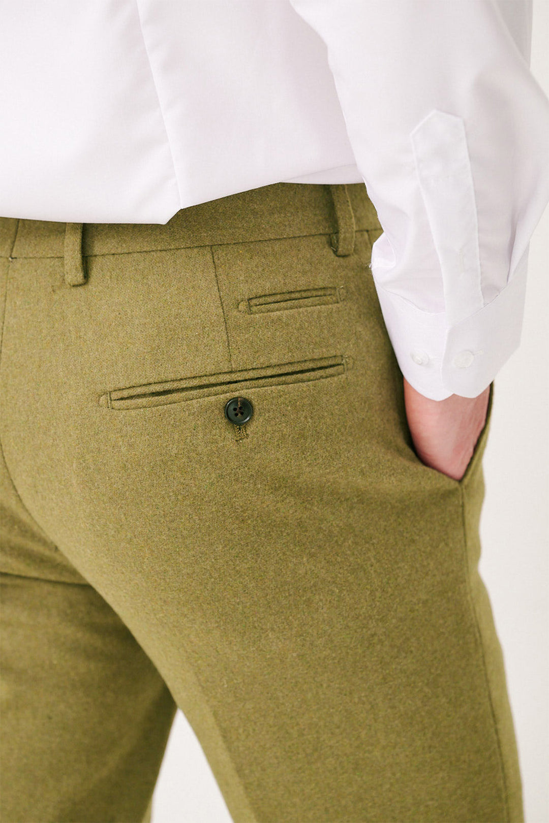 A person models the marcdarcy ARCHIE - Moss Tweed Trousers, paired with a white dress shirt and one hand in their pocket, showcasing the slim fit's back buttoned pocket.