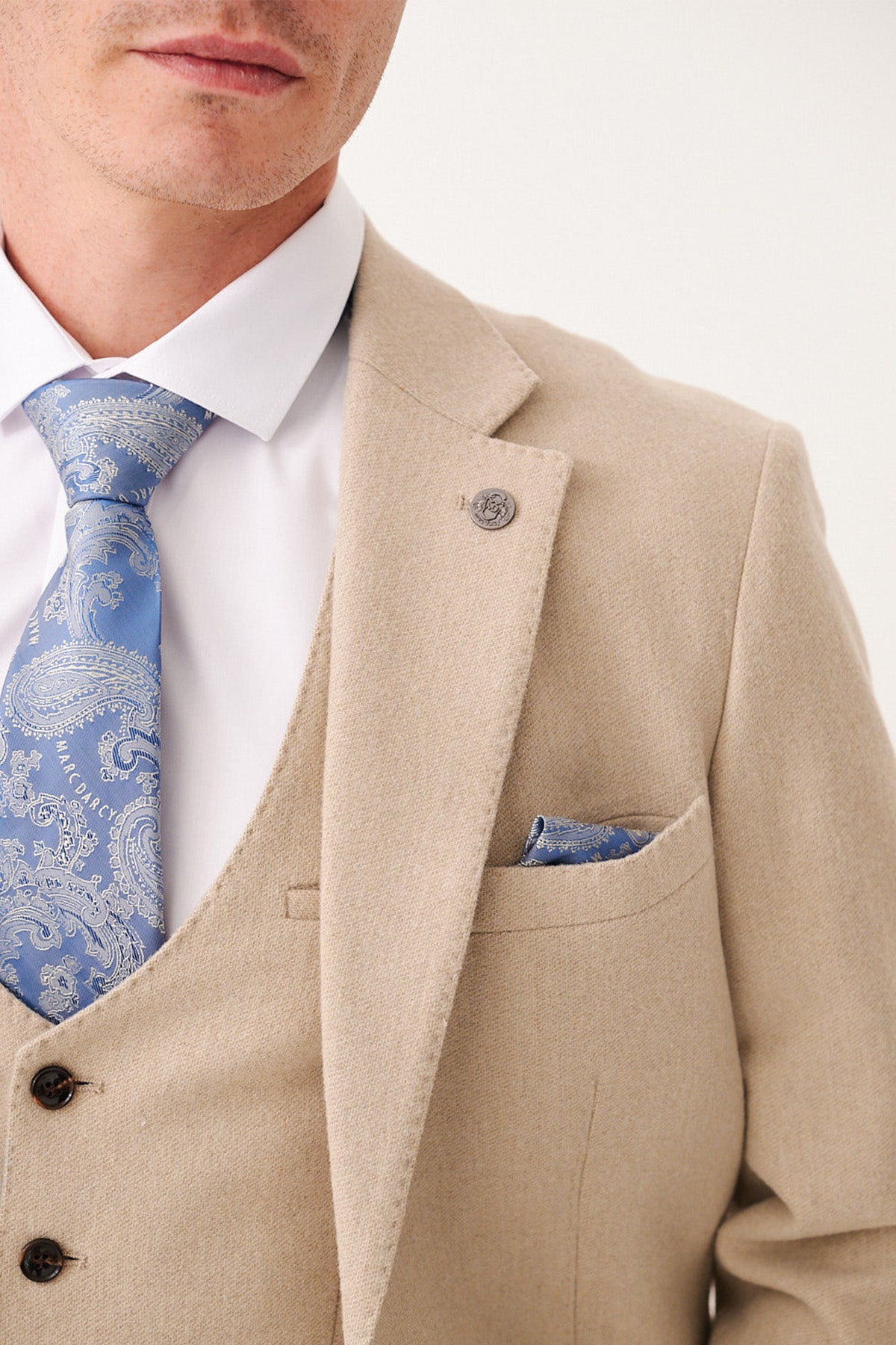 A man wearing the marcdarcy ARCHIE - Stone Tweed Blazer, a white shirt, and a blue patterned tie with a matching blue pocket square. Only his lower face and upper body are visible.