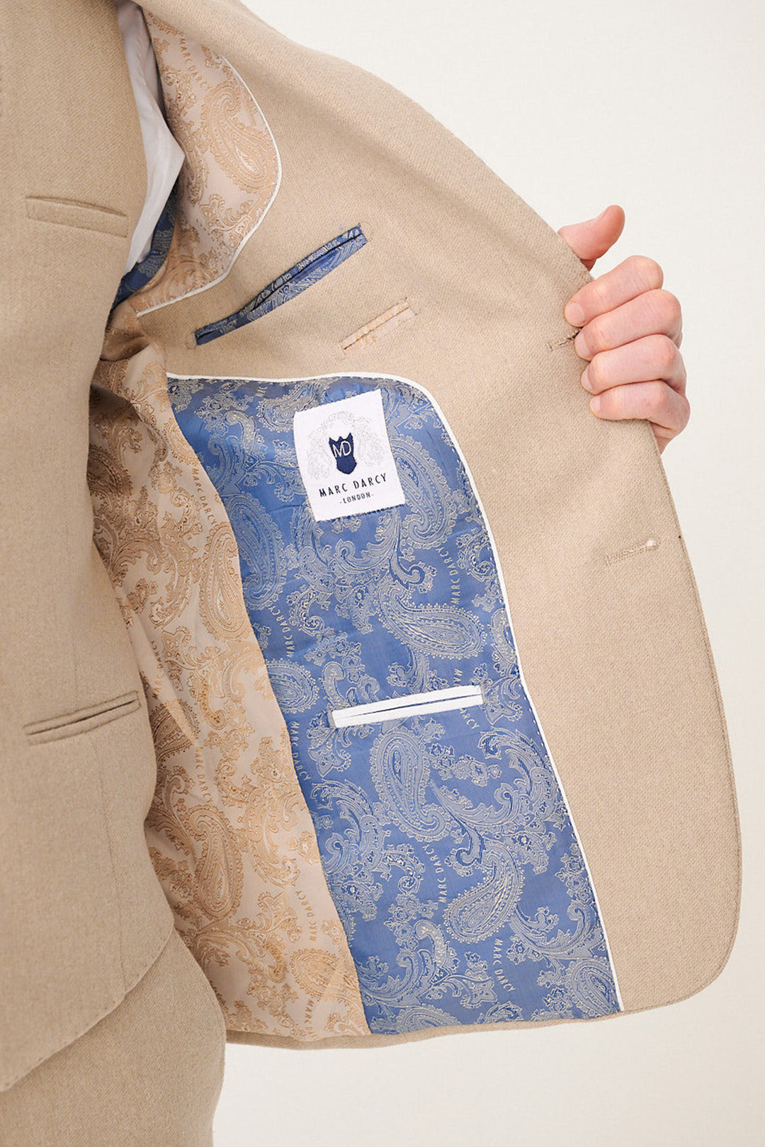 A person holds open the marcdarcy ARCHIE Stone Tweed Three Piece Suit jacket, revealing its gold and blue paisley inner lining, an inner pocket, and the brand label. The slim fit jacket showcases classic elegance throughout.
