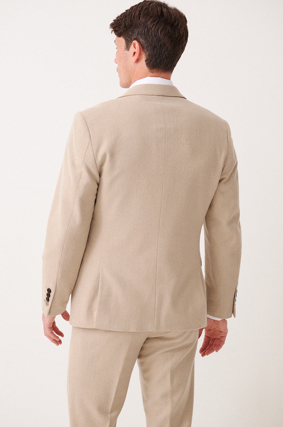 A man models the marcdarcy ARCHIE - Stone Tweed Blazer, standing with his back to the camera to reveal the suit jacket and matching trousers. His head is slightly turned left, arms relaxed at his sides.