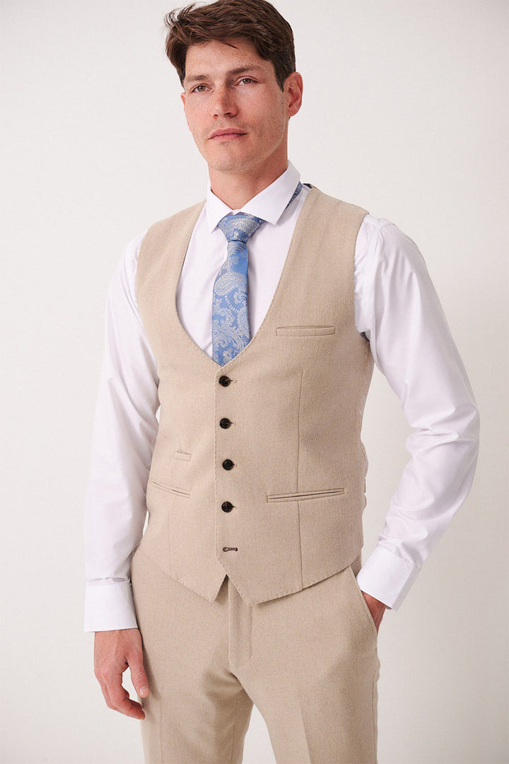 A man in a Marc Darcy ARCHIE - Stone Tweed Waistcoat and matching trousers over a white dress shirt with a light blue patterned tie, standing against a plain light background.