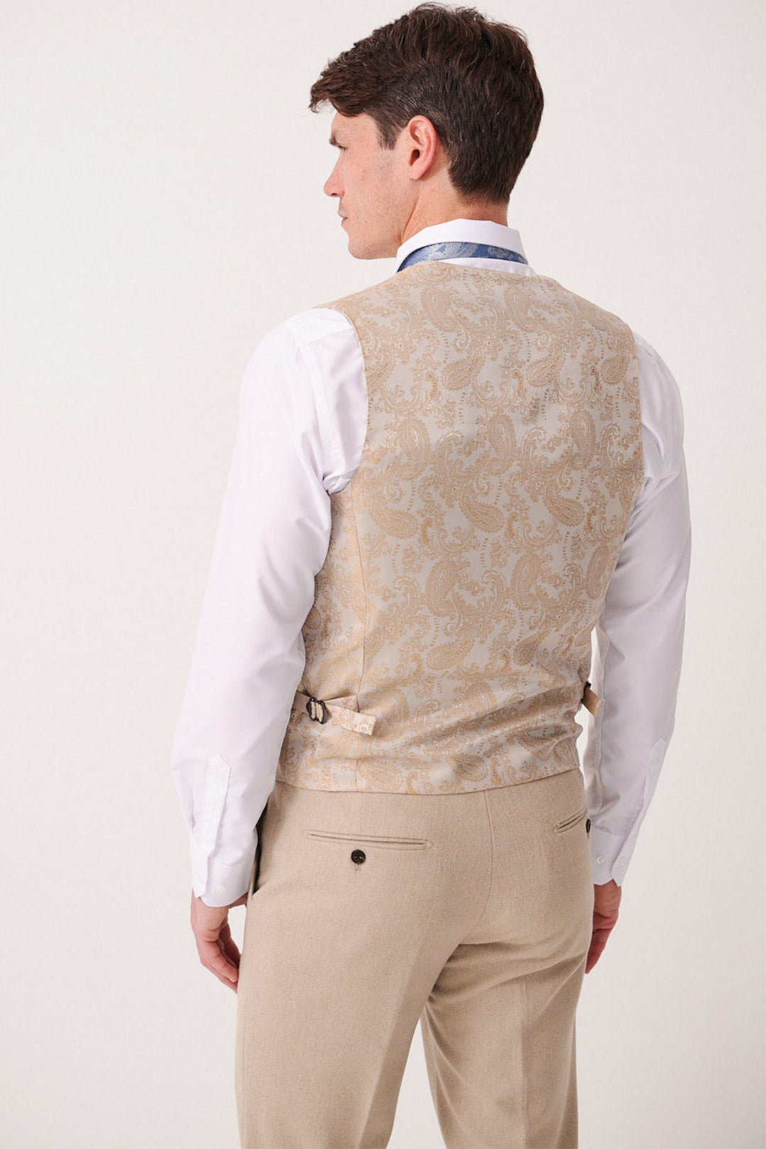 A man is seen from behind wearing the marcdarcy ARCHIE - Stone Tweed Three Piece Suit, featuring a slim fit vest with adjustable side straps over a white dress shirt and beige trousers.
